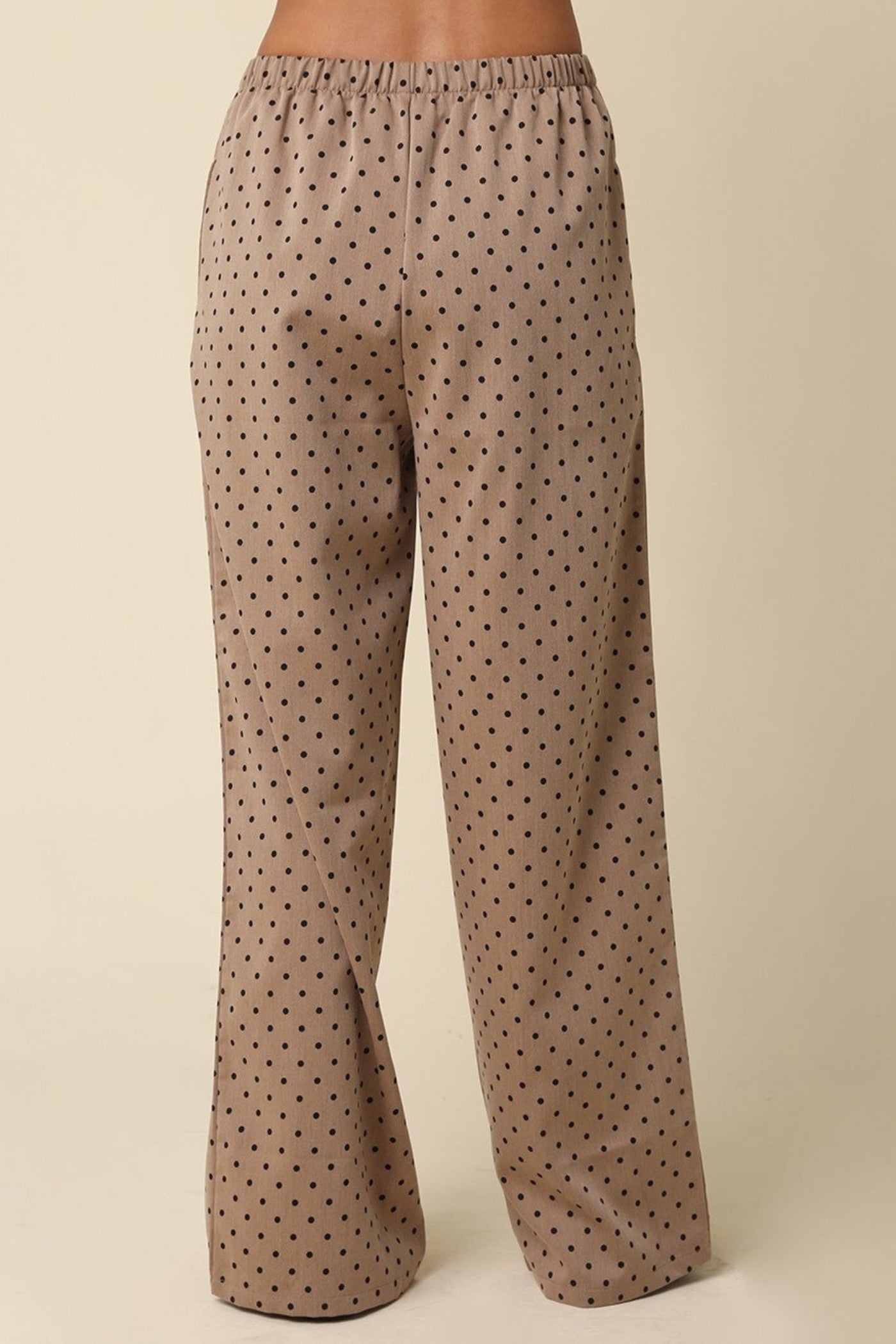 A pair of wide-leg pants in a taupe-brown fabric with a small black polka dot pattern, shown on a model from the waist down against a solid beige background.