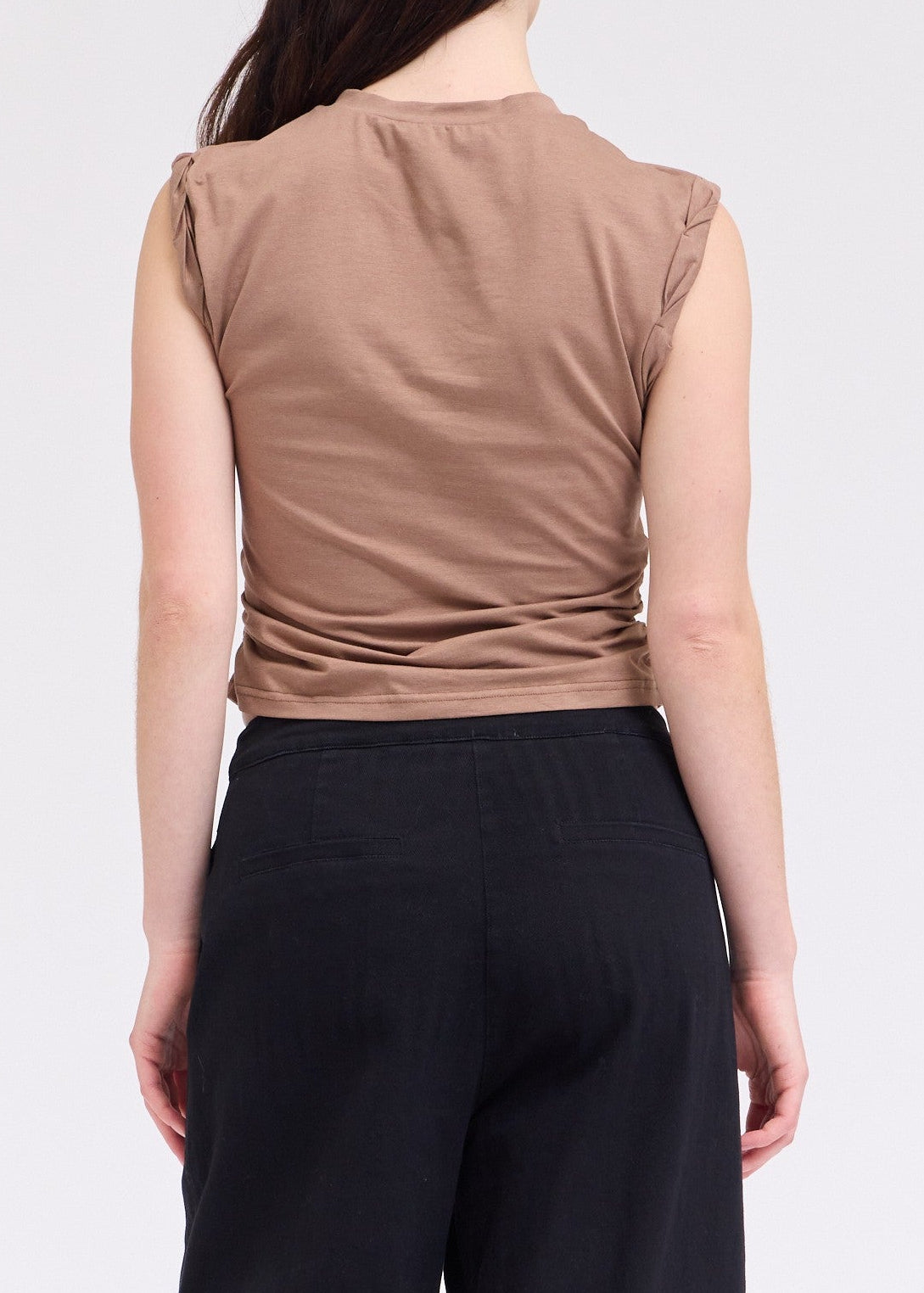 Woman wearing a brown sleeveless top and black pants on a white background