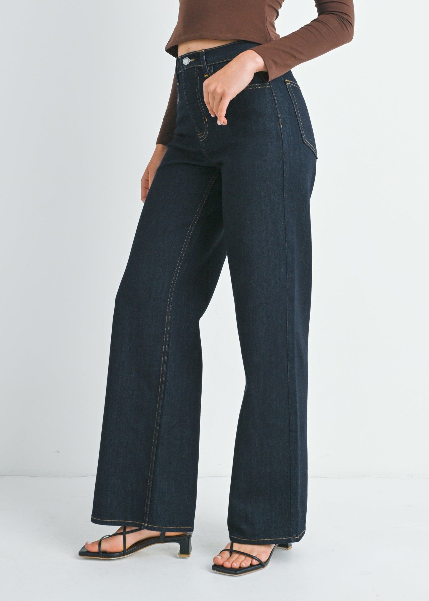 Woman wearing a brown off-shoulder top and dark blue jeans on a white background