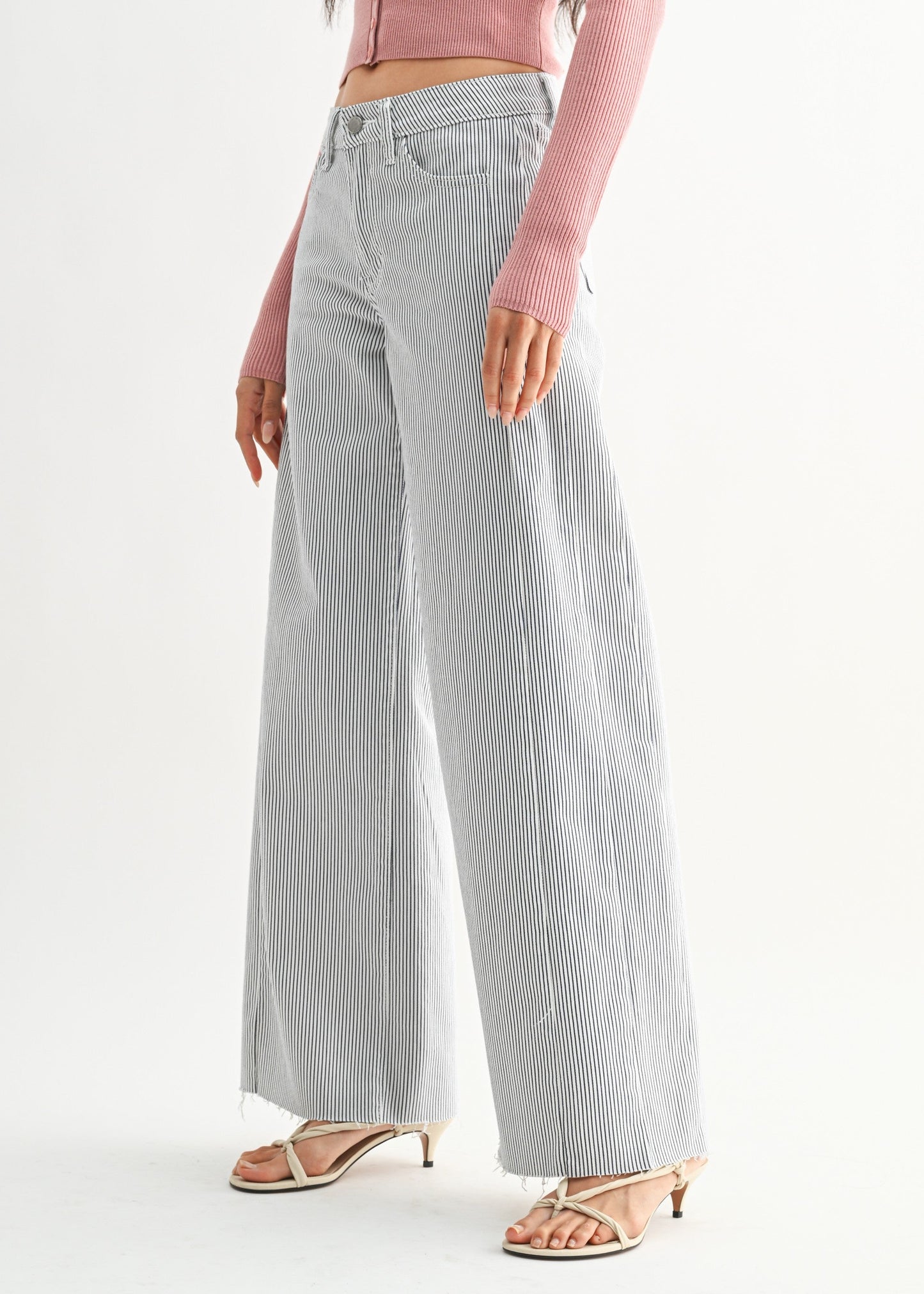 Woman wearing a pink cardigan and light gray pants on a white background