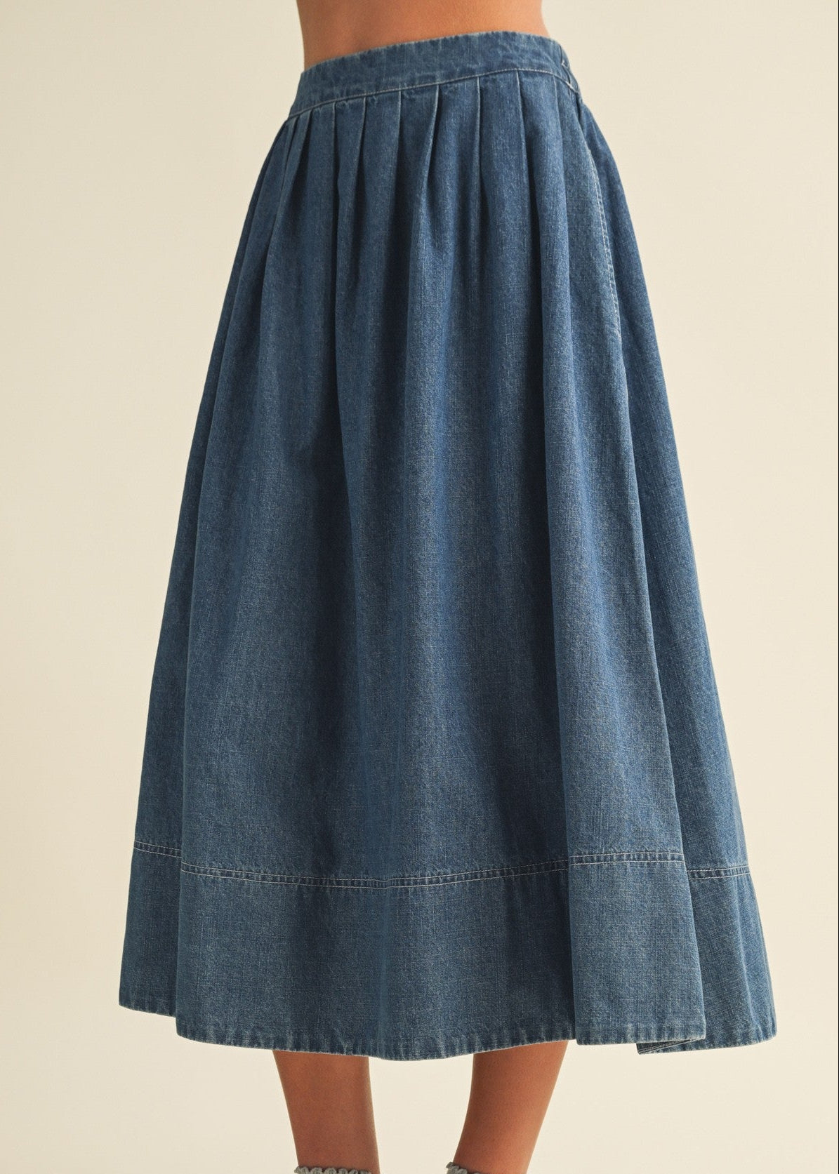 Person wearing a blue denim skirt on a beige background