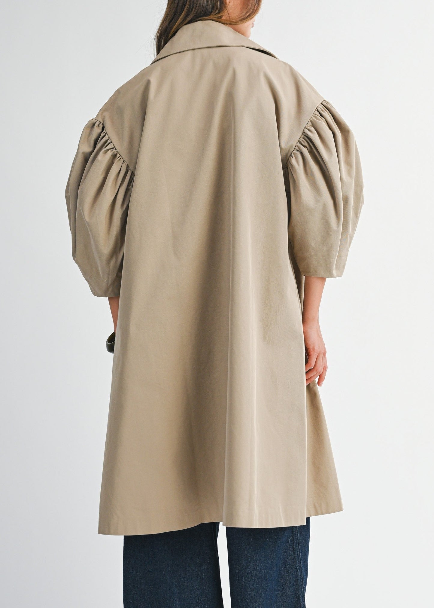 Person wearing a beige trench coat on a white background