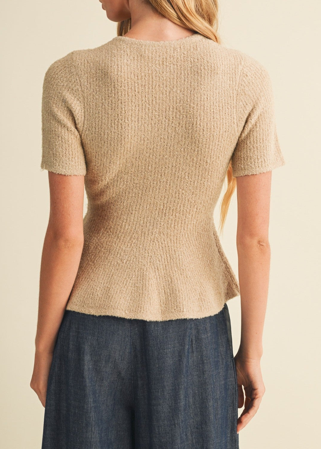 A woman shown from the back wearing a short-sleeve ribbed knit top in a light beige color, paired with dark blue wide-leg pants, against a plain cream background.